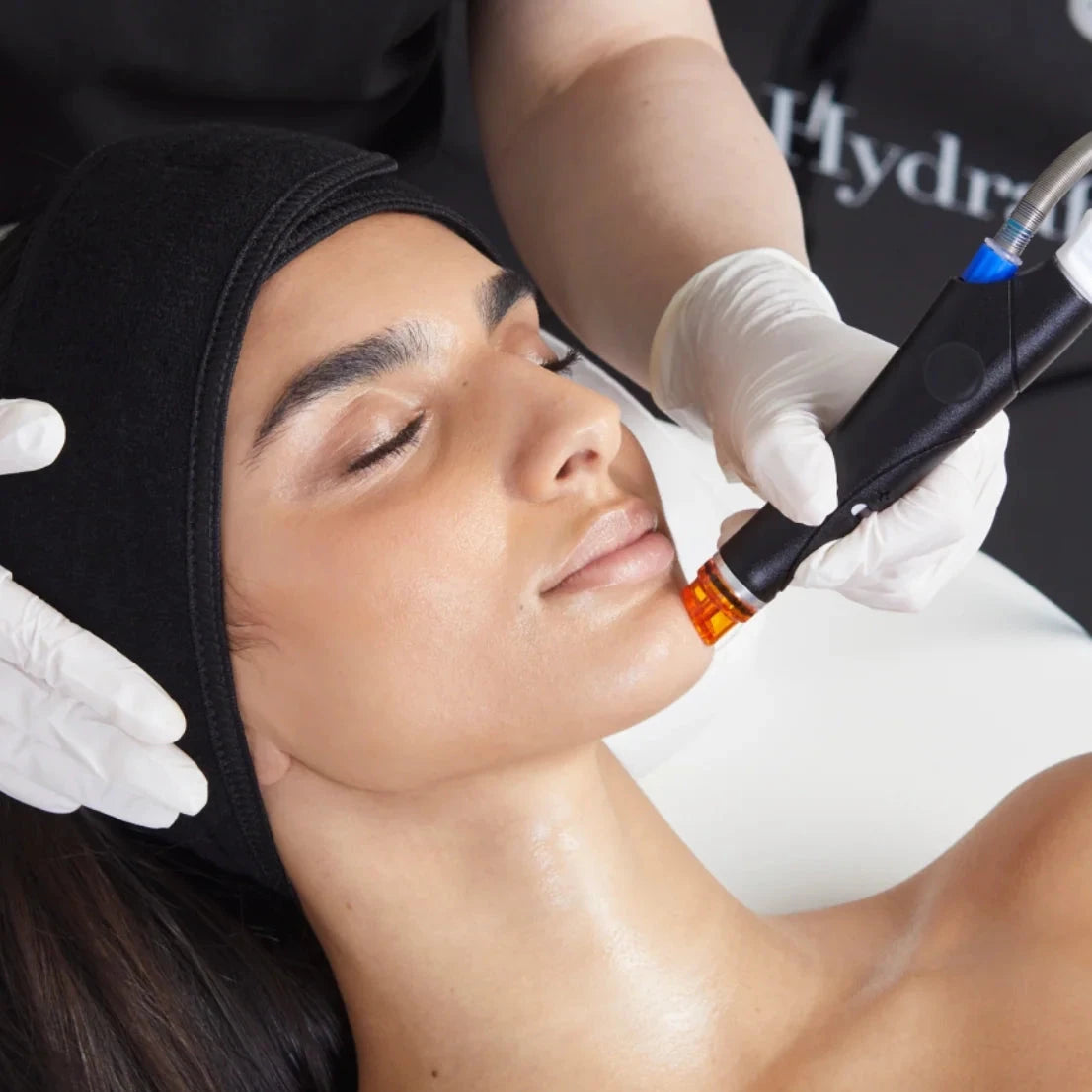 Woman receiving a facial treatment with a device, wearing a black hood and gloves.