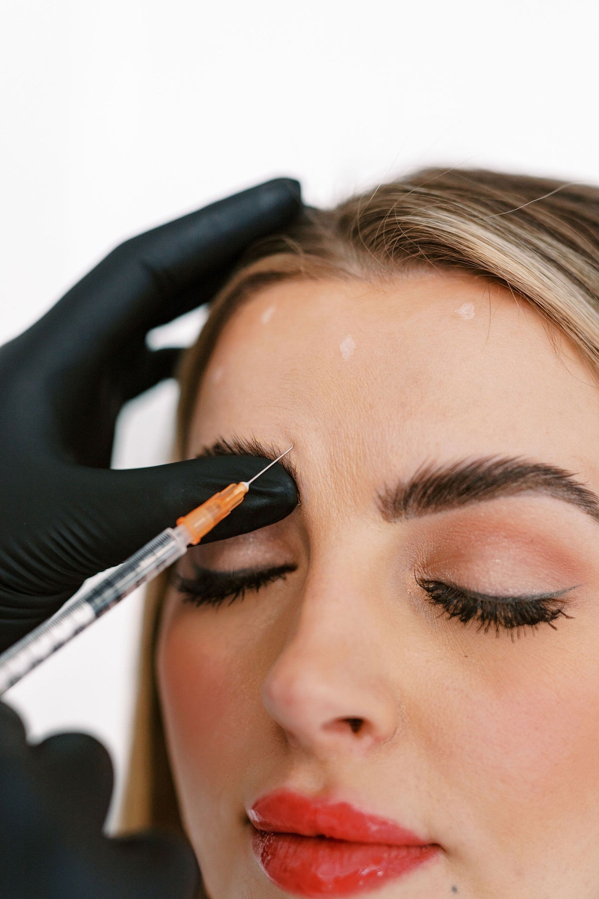 Person receiving an injection on the face with a black glove